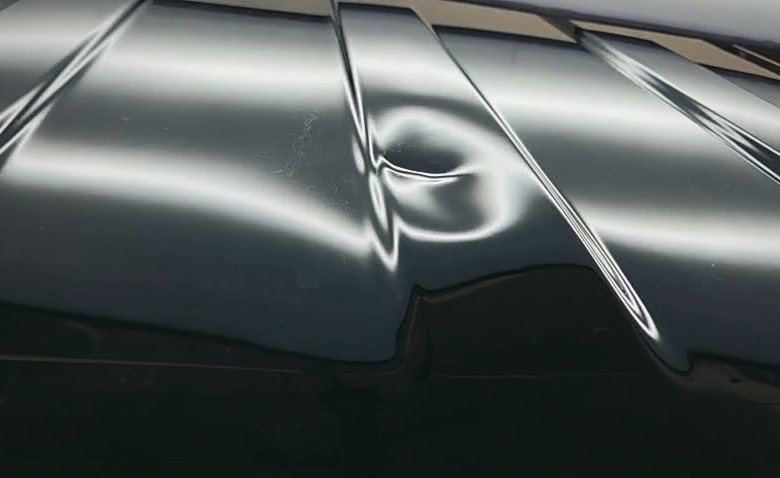 Real photo: a dent bending the reflected lines of a light board